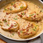 Pinterest graphic of Marry Me Chicken. Image shows skillet of Marry Me Chicken topped with fresh basil with two glasses of red wine sitting in background. Text says "super easy Marry Me Chicken simplejoy.com"