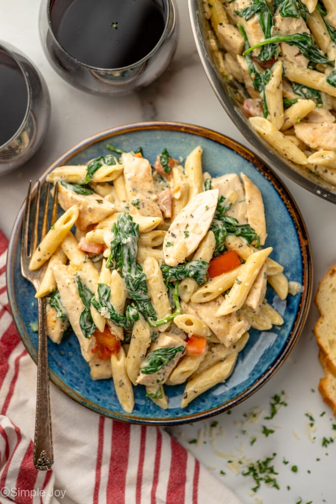 Overhead view of a plate of Chicken Penne Pasta with a fork, glasses of red wine beside