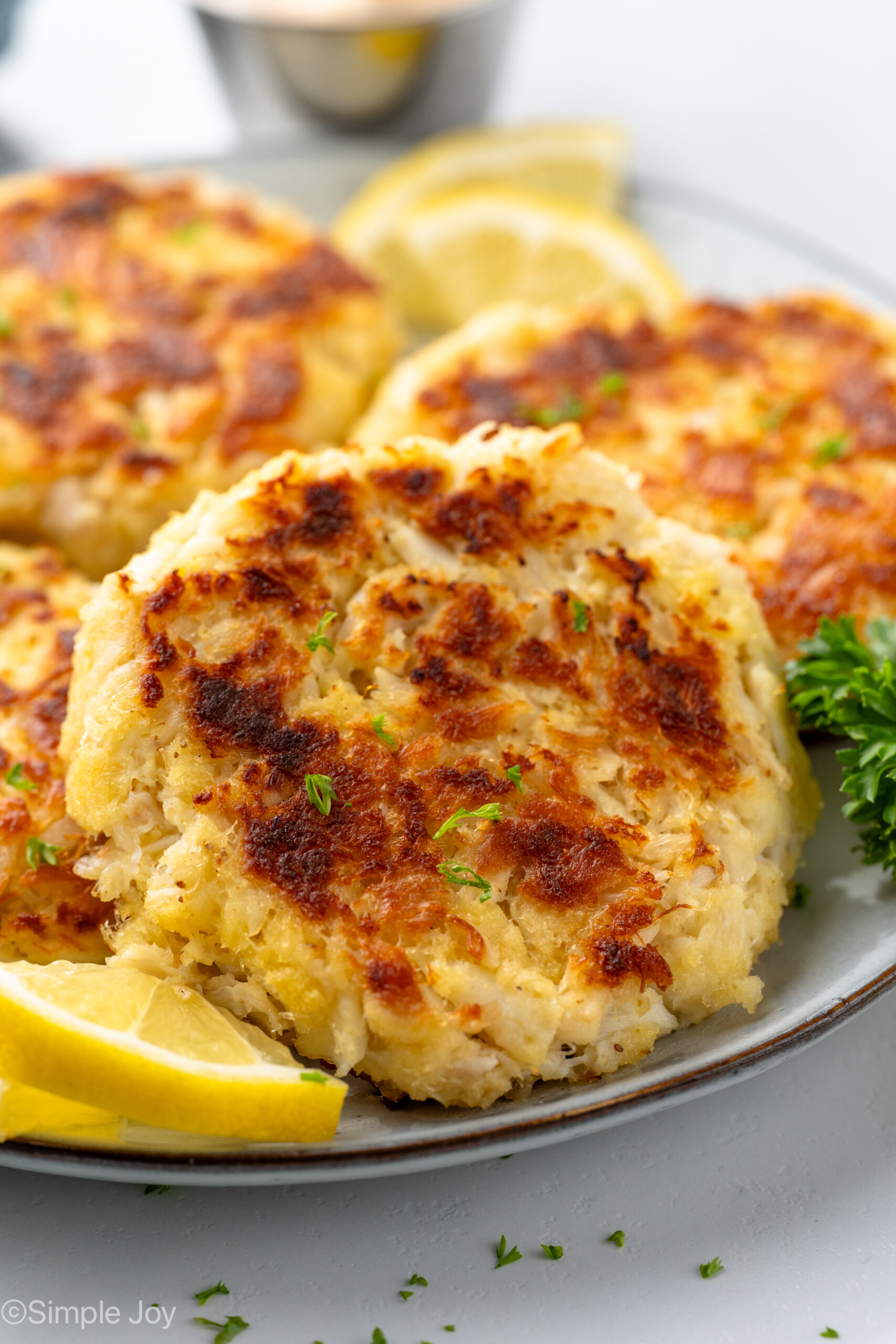 close up of crab cakes on a plate with fresh parsley and lemon slices