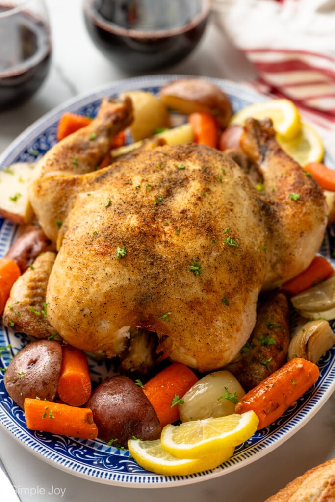 Crockpot Whole Chicken on a platter surrounded by red potatoes, carrots, onion, and lemon slices.