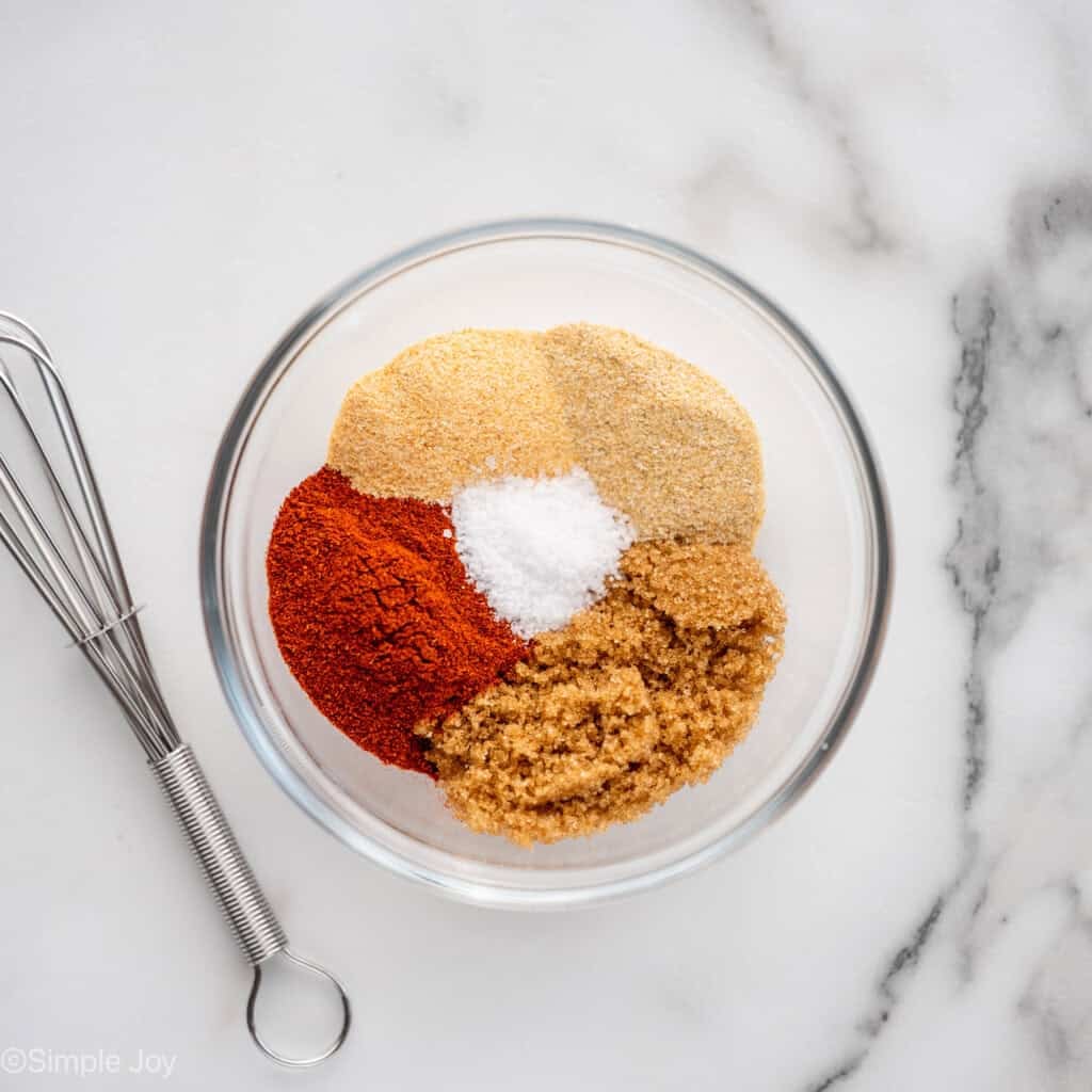 overhead of glass bowl of seasonings and spices with a wire whisk sitting beside to make Baked Pork Chops