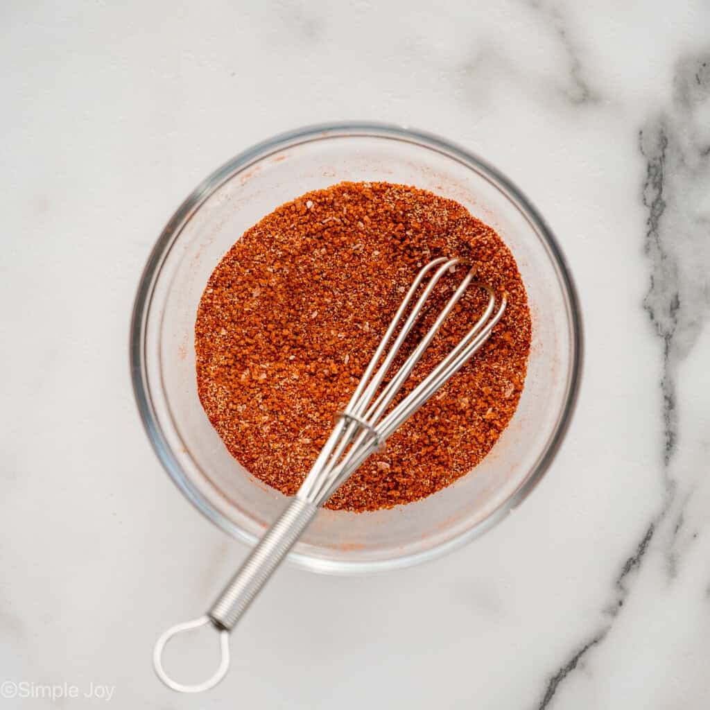 overhead of class bowl of seasonings and whisk to make Baked Pork Chops