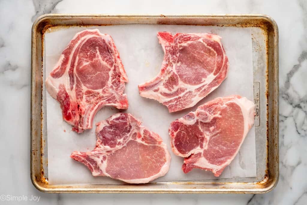 overhead of raw pork chops on a parchment-lined baking sheet to make Baked Pork Chops
