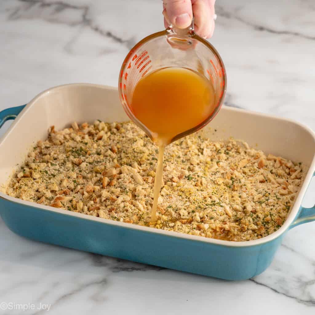 person's hand pouring measuring cup of ingredients over baking dish of stuffing mix for Chicken and Stuffing Casserole recipe