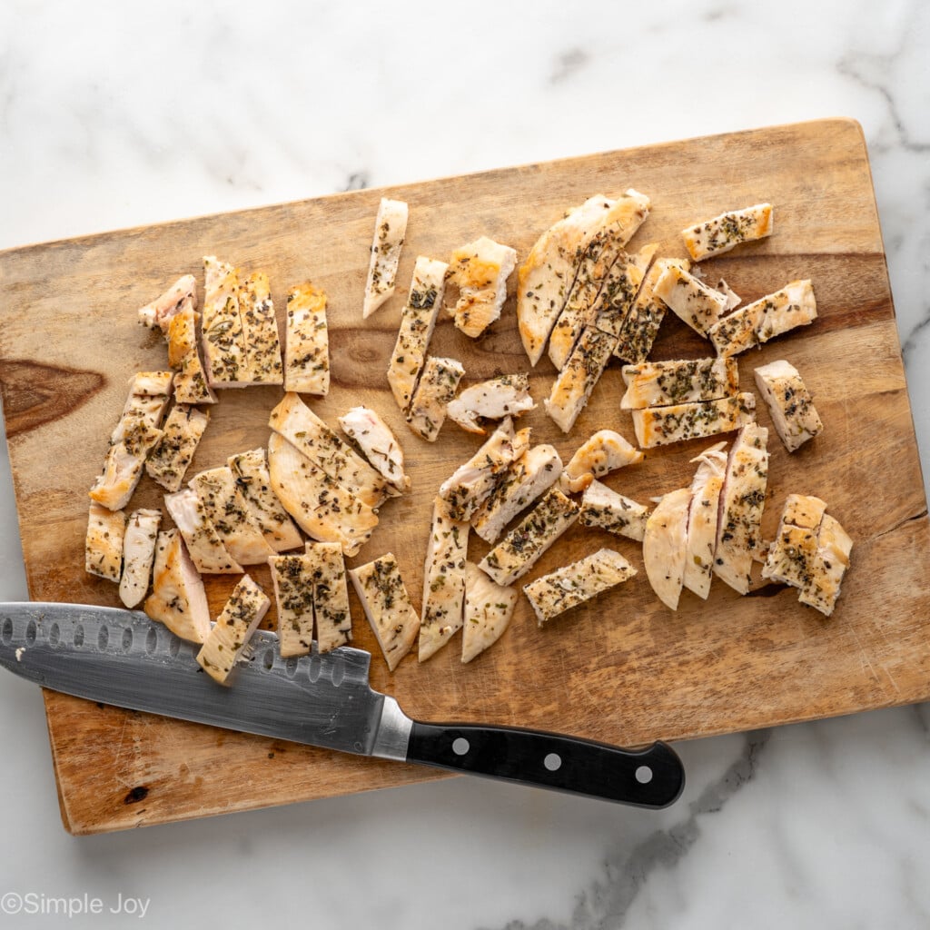 Overhead view of a cutting board with diced chicken and a knife for Chicken Penne Pasta recipe