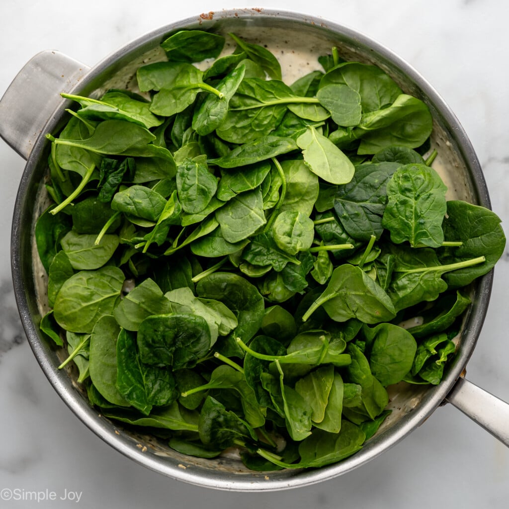 Overhead view of a skillet topped with spinach for Chicken Penne Pasta reicpe