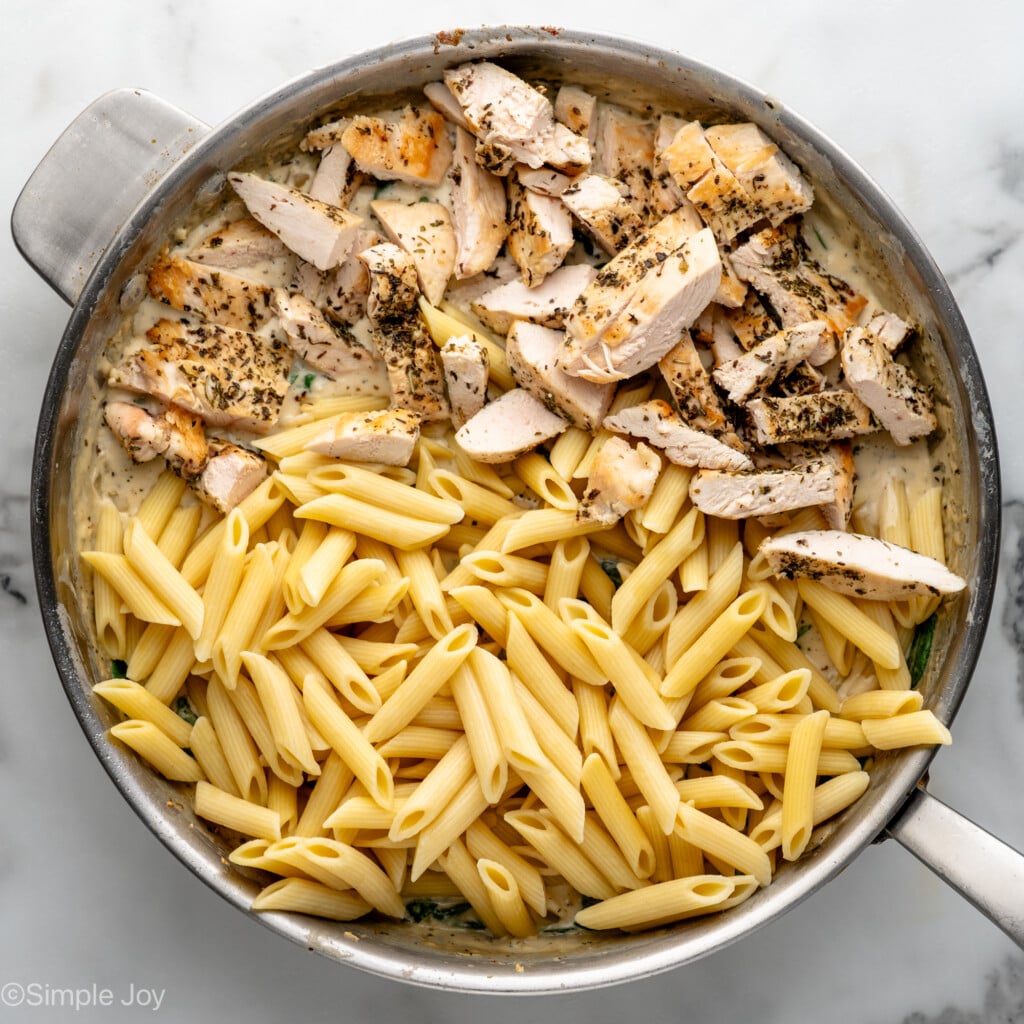 Overhead view of a skillet of noodles, diced chicken, and other ingredients for Chicken Penne Pasta recipe