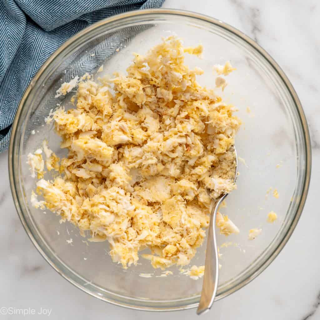 overhead of glass bowl of crab cakes ingredients with a spoon