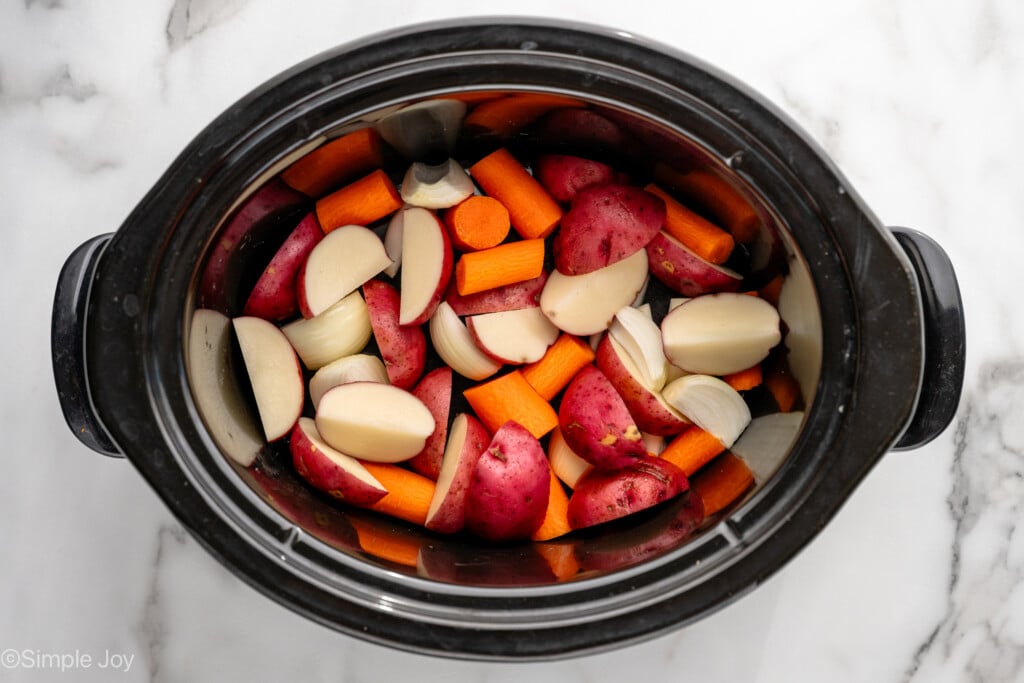overhead of slow cooker of diced red potatoes, carrots, and onion for making Crockpot Whole Chicken