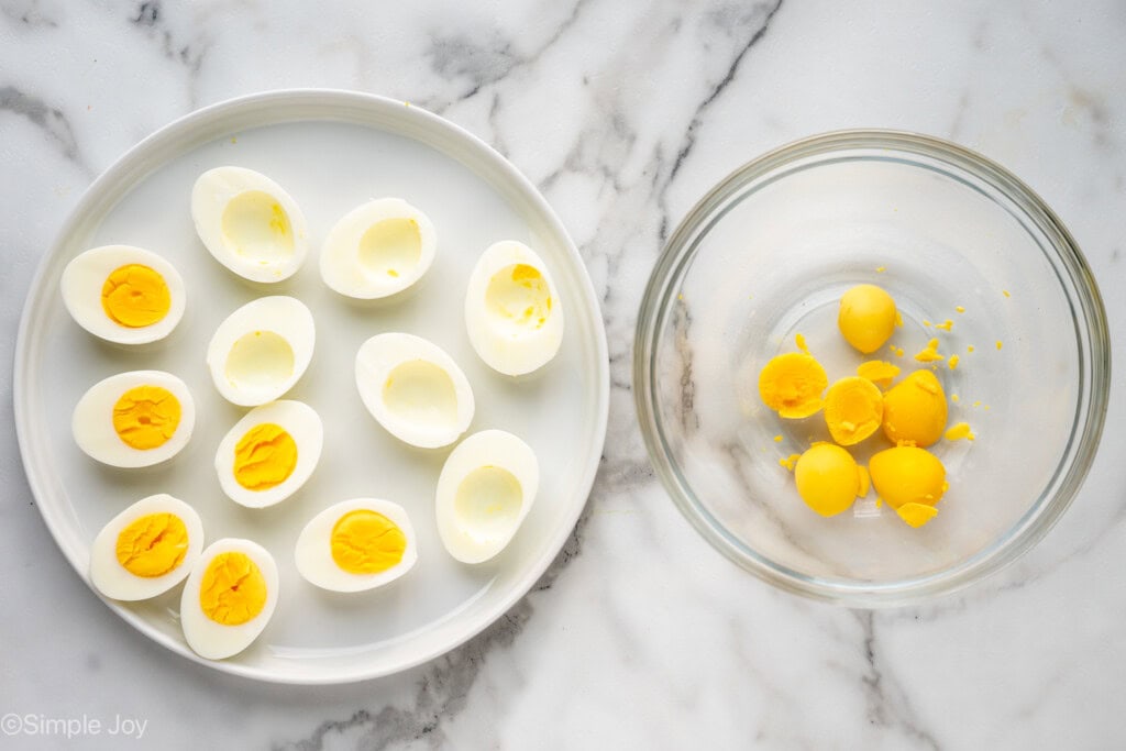 Overhead view of a plate of hard boiled eggs cut in half with bowl beside with yolks for Deviled Eggs with Bacon recipe