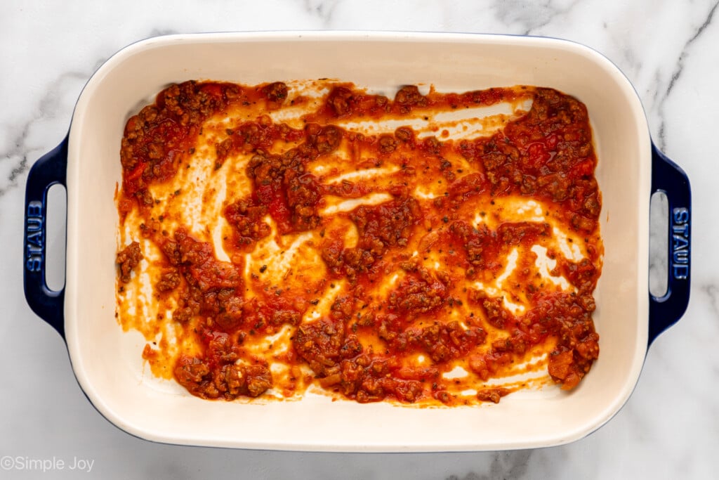 Overhead view of baking dish with sauce spread on bottom for Lasagna Roll Ups recipe