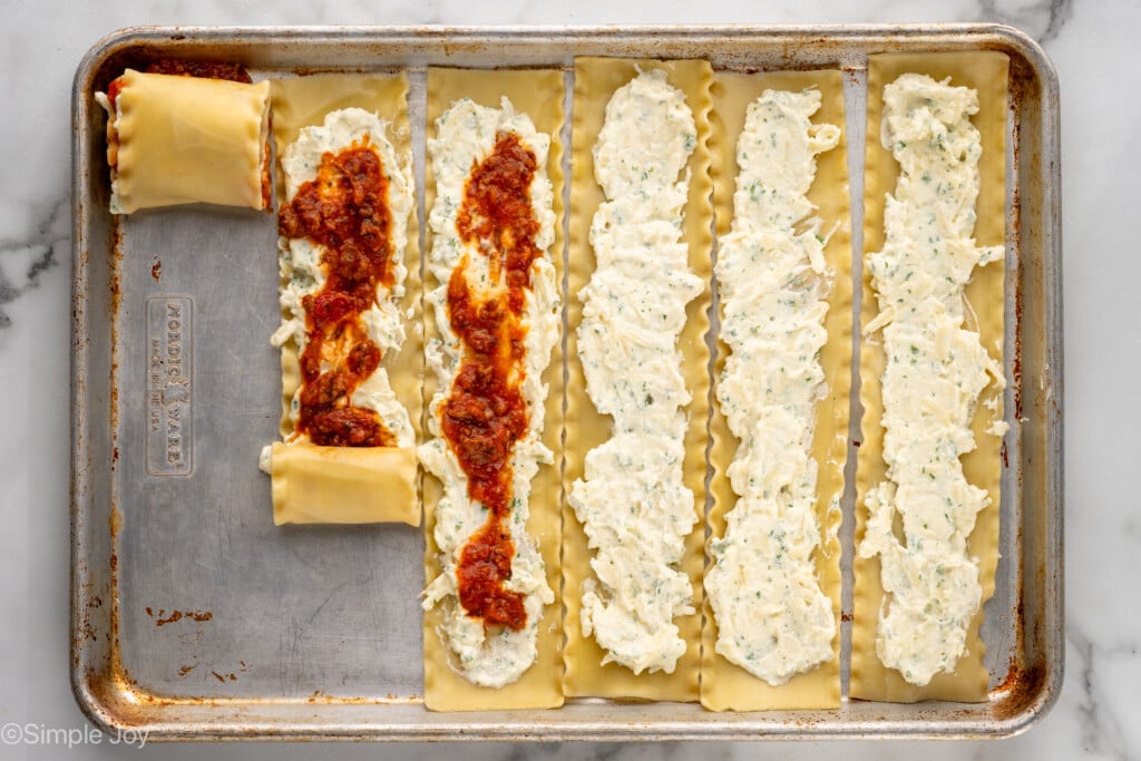 Overhead view of a baking sheet with lasagna noodles with some filling on them for Lasagna Roll Ups recipe