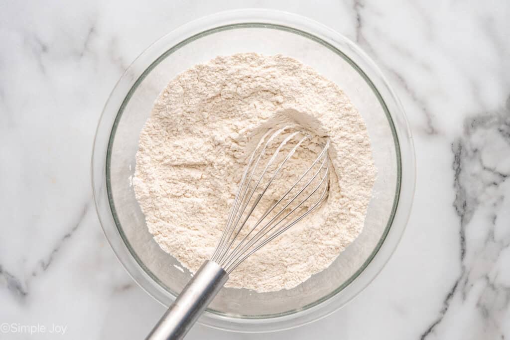 Overhead view of a mixing bowl of dry ingredients and a whisk for Lemon Sugar Cookie Bars recipe