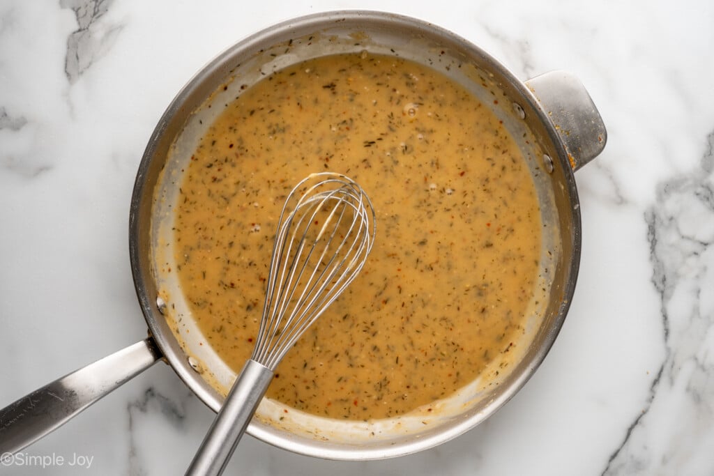 Overhead of skillet of Marry Me Chicken sauce ingredients with a whisk