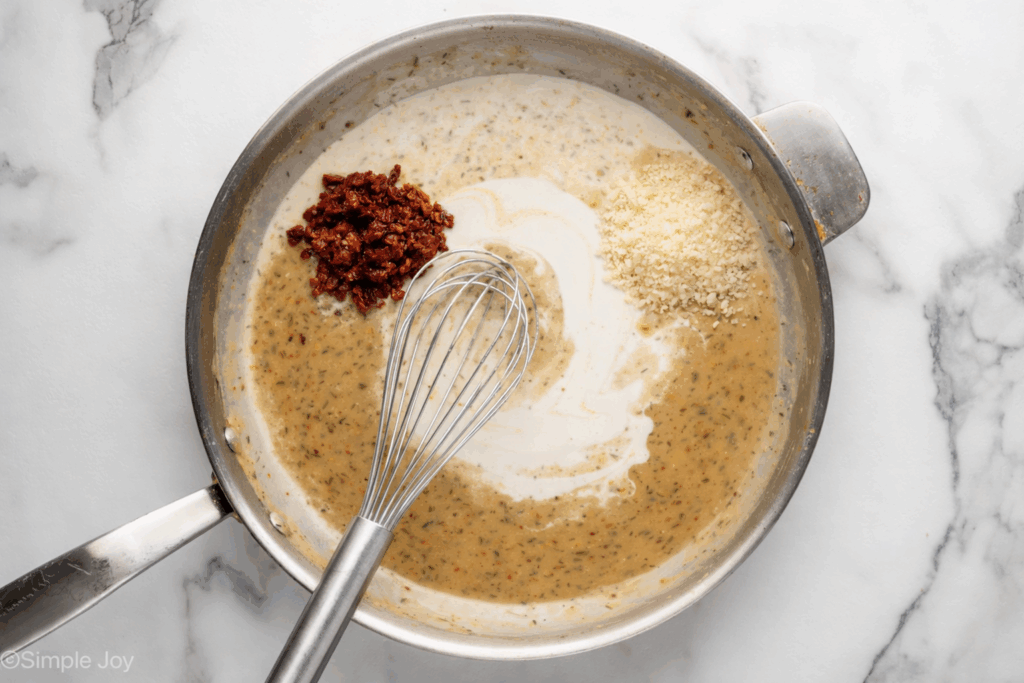Overhead of skillet of Marry Me Chicken sauce ingredients and a whisk