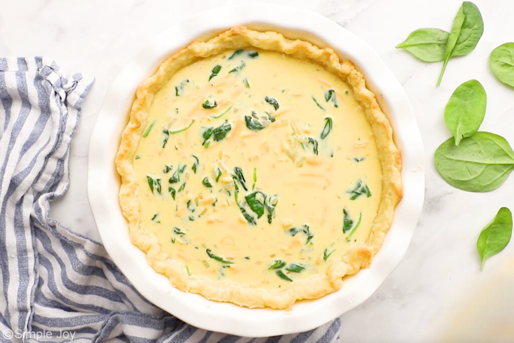 overhead of spinach quiche in a pie plate with spinach sitting beside