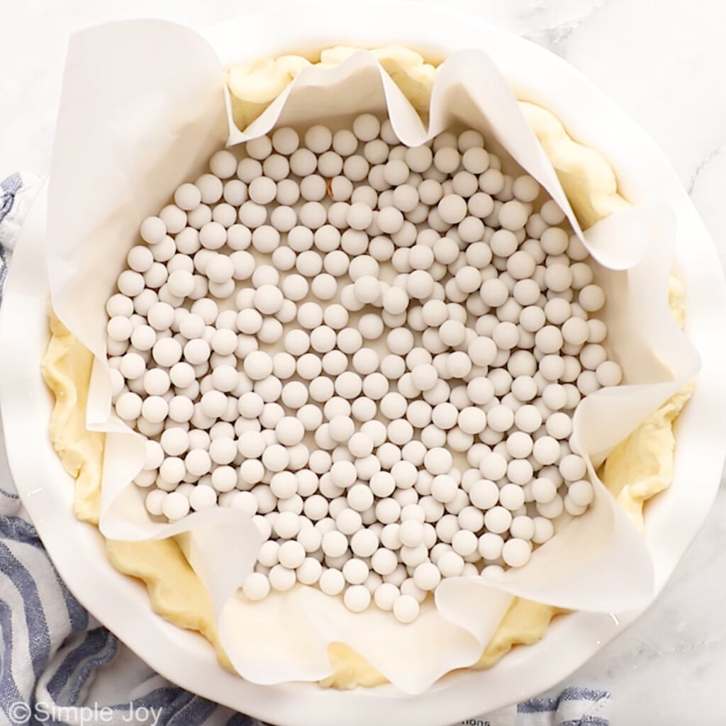 Overhead of homemade pie crust with parchment paper and pie weights to make spinach quiche