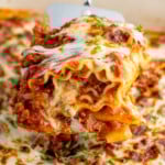 Serving spatula lifting Lasagna Roll Up from baking dish of Lasagna Roll Ups recipe, garnished with fresh parsley