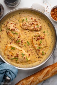 Overhead of skillet of Marry Me Chicken with baguette sitting beside