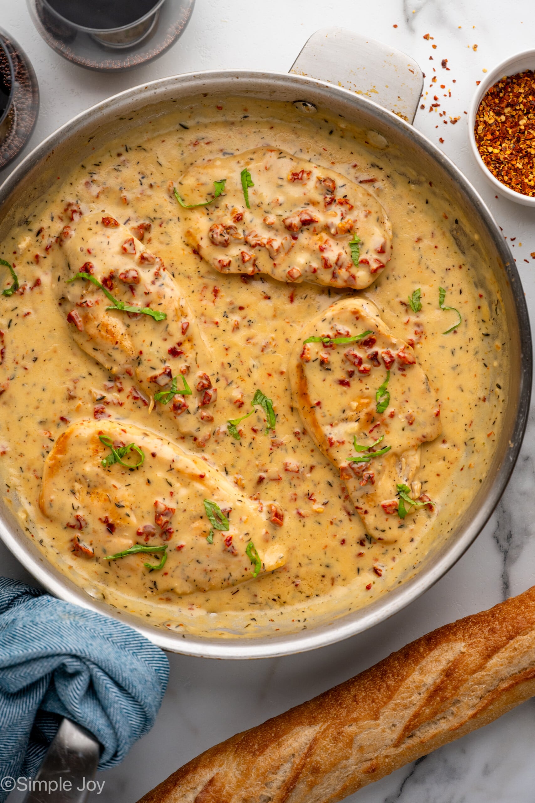 Overhead of skillet of Marry Me Chicken with baguette sitting beside