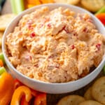 Bowl of Pimento Cheese recipe surrounded by crackers and sliced vegetables