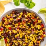Pinterest graphic for Black Bean and Corn Salsa. Says "the best Black Bean and Corn Salsa simplejoy.com" Image shows overhead of bowl of Black Bean and Corn Salsa with lime slices and tortilla chips sitting beside.