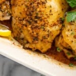 Pinterest graphic for Greek Chicken. Image shows close up of Greek Chicken garnished with lemon slices and fresh parsley. Says "super easy Greek Chicken simplejoy.com"