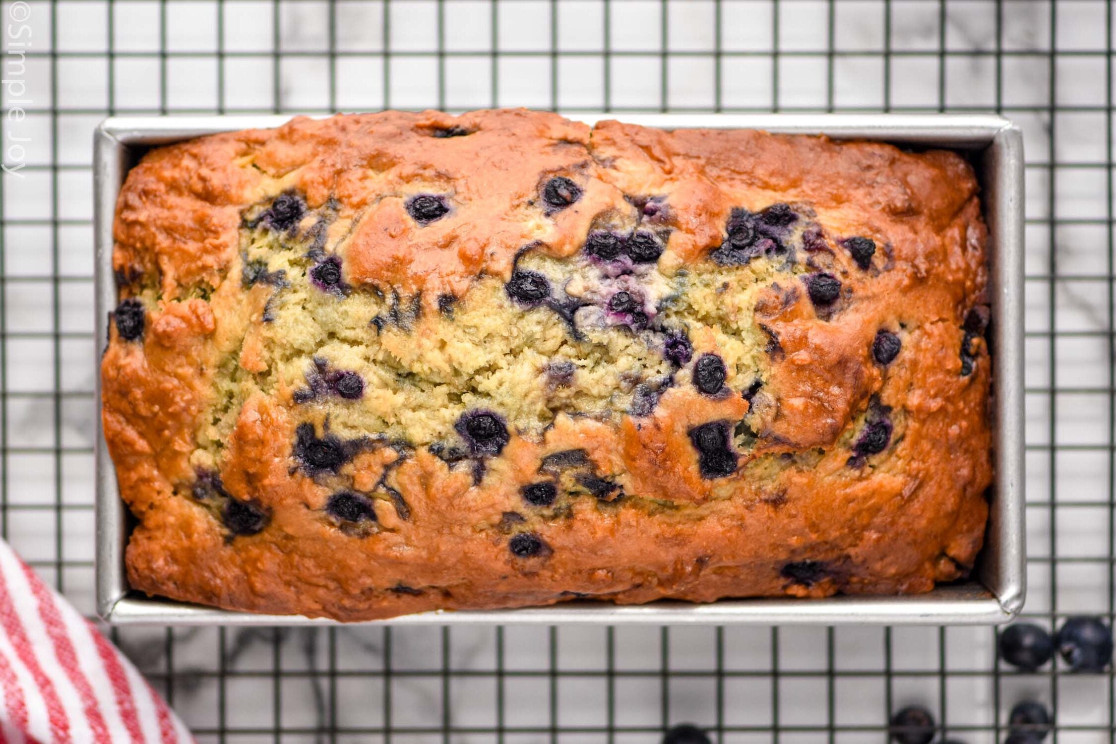 overhead of banana bread with blueberries in a bread pan on a cooling rack