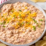 Bowl of Boat Dip garnished with shredded cheese and diced chives, potato chips sitting beside