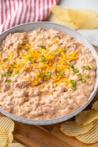Bowl of Boat Dip garnished with shredded cheese and diced chives, potato chips sitting beside