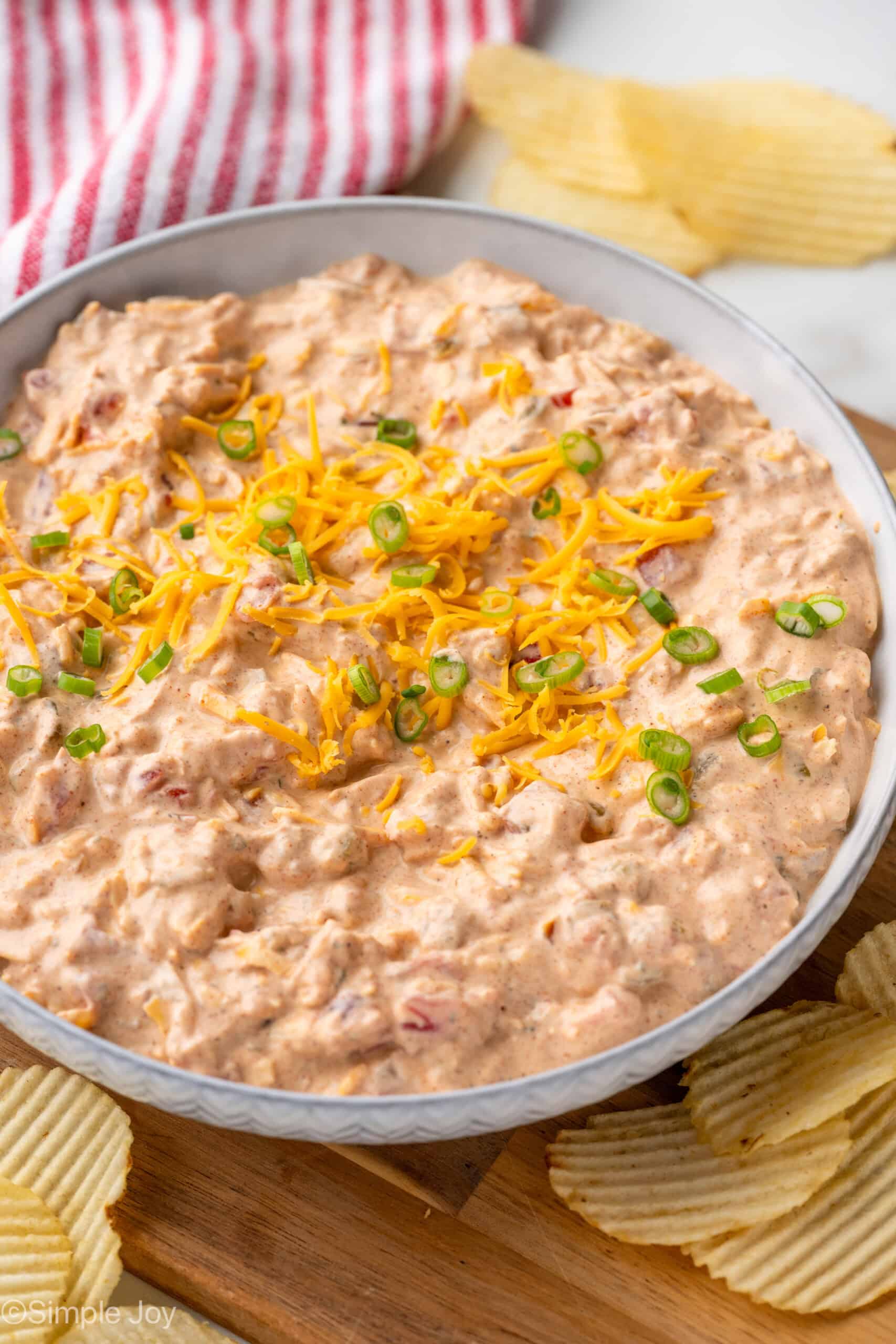 Bowl of Boat Dip garnished with shredded cheese and diced chives, potato chips sitting beside