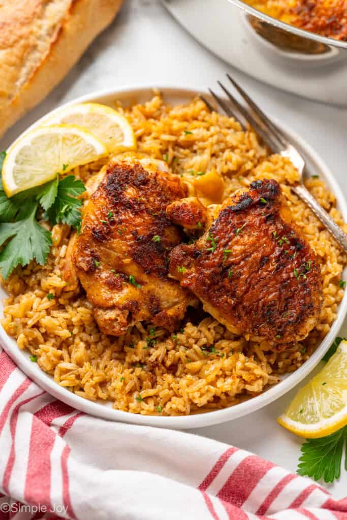 White plate of Chicken and Rice with fork, garnished with lemon slices and parsely.