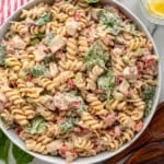 overhead of white bowl full of chicken pasta salad, glasses of water with lemon slices and spoons sitting beside