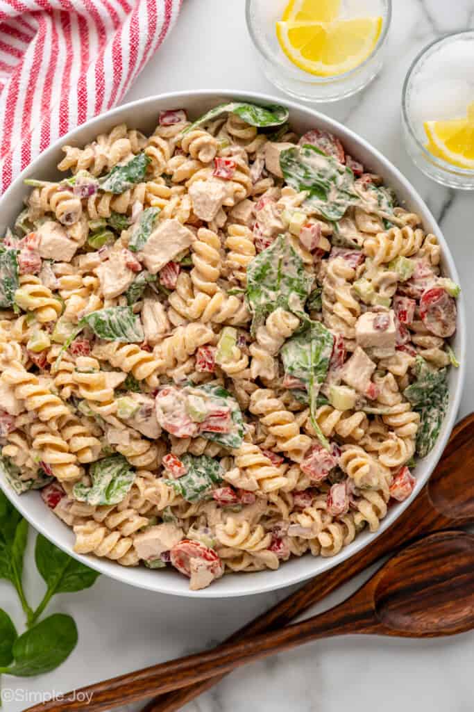 overhead of white bowl full of chicken pasta salad, glasses of water with lemon slices and spoons sitting beside