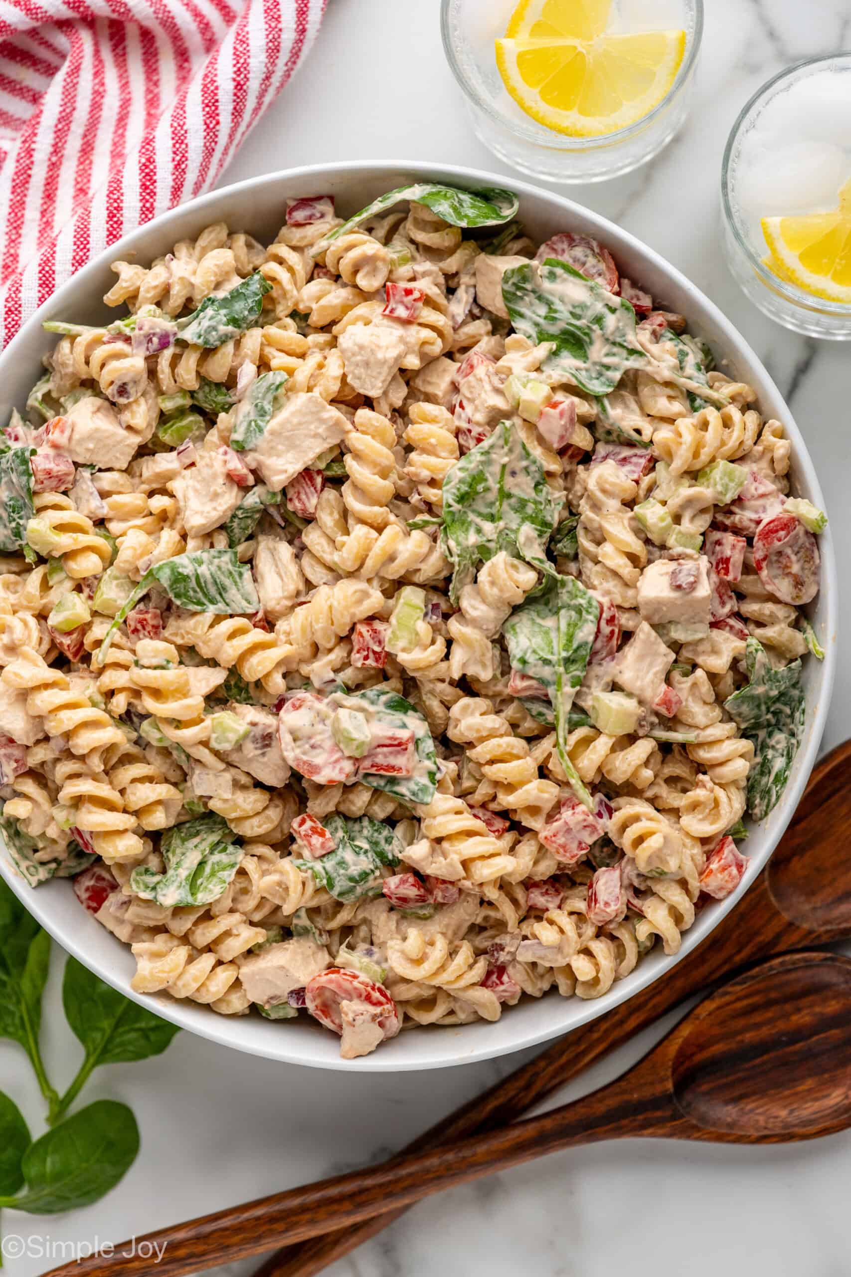 overhead of white bowl full of chicken pasta salad, glasses of water with lemon slices and spoons sitting beside
