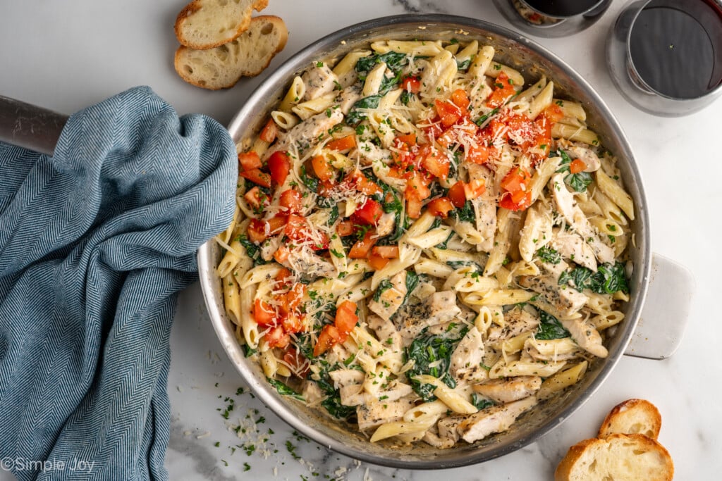 overhead of a skillet of chicken penne pasta garnished with tomatoes and parmesan