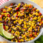 Bowl of Black Bean and Corn Salsa with lime wedges, fresh cilantro, and tortilla chips surrounding