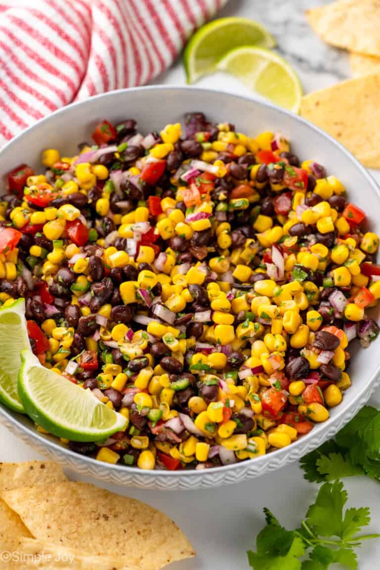 Bowl of Black Bean and Corn Salsa with lime wedges, fresh cilantro, and tortilla chips surrounding