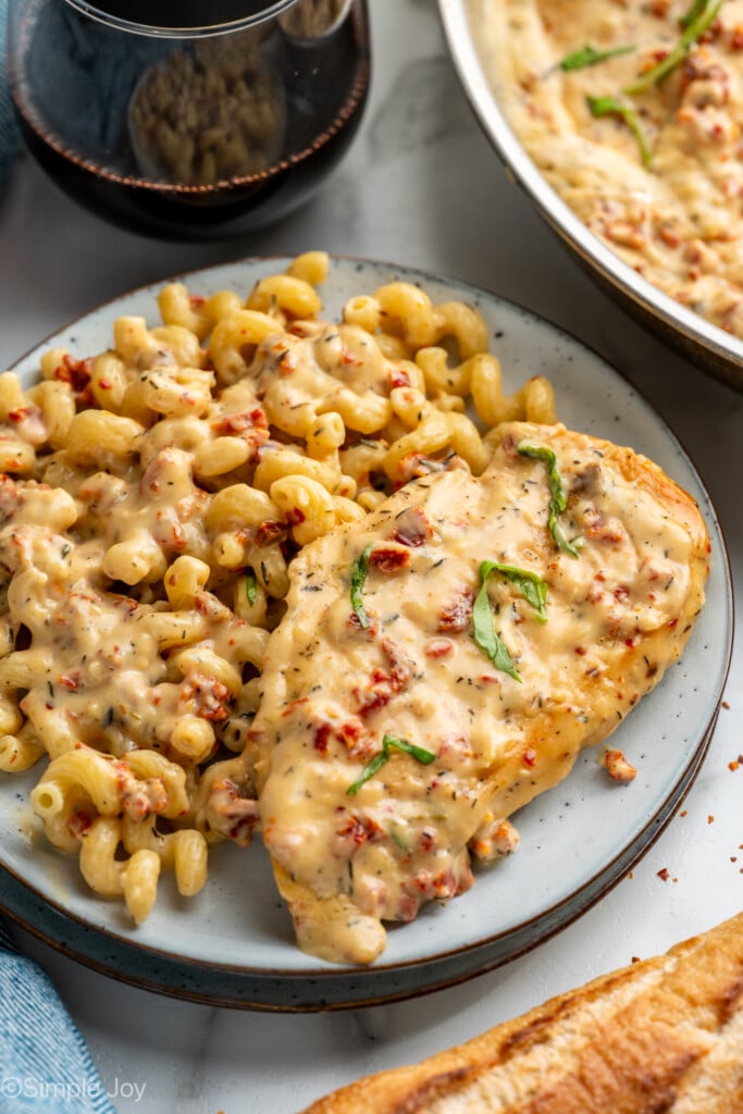 plate of marry me chicken and pasta with glass of red wine sitting beside