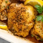 Close up of Greek Chicken in a baking dish garnished with lemon slices and parsley