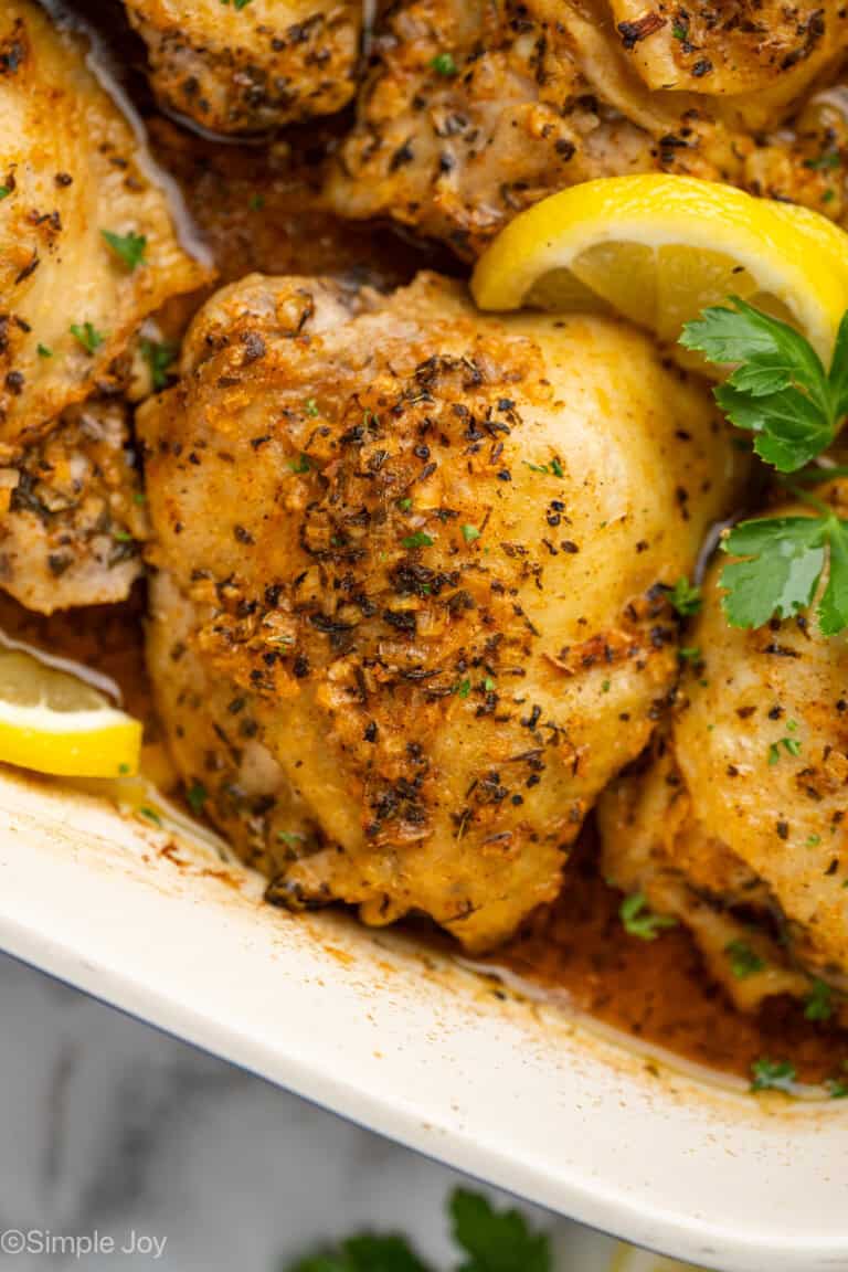 Close up of Greek Chicken in a baking dish garnished with lemon slices and parsley