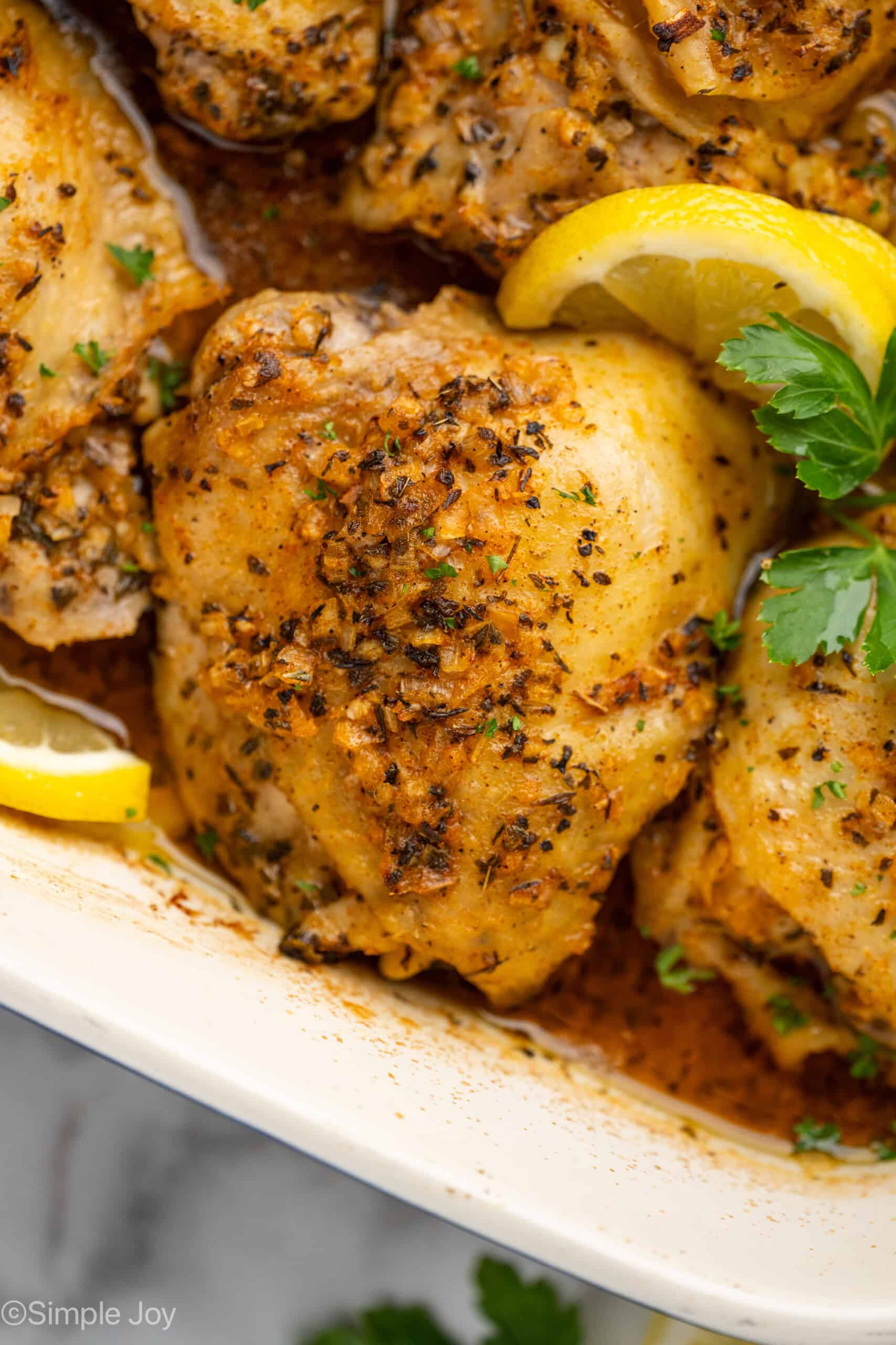 Close up of Greek Chicken in a baking dish garnished with lemon slices and parsley