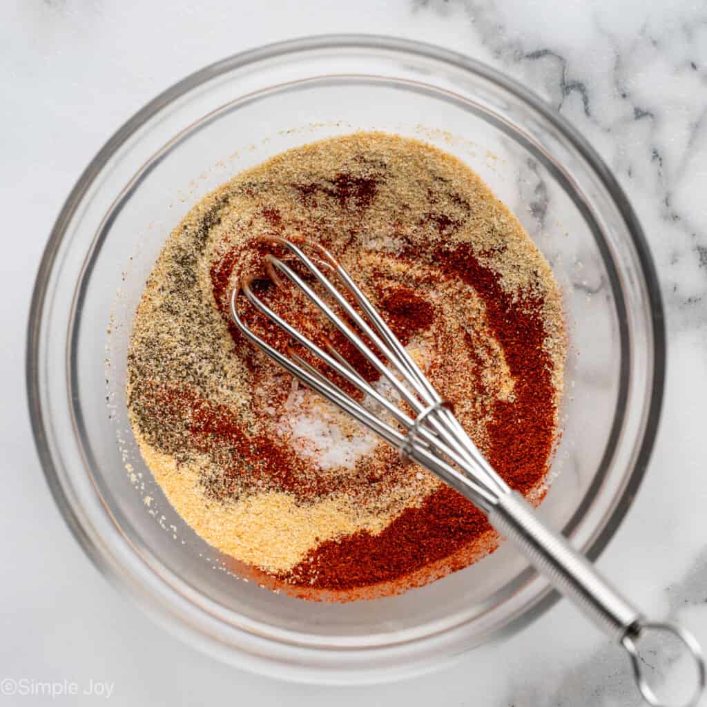 Overhead of glass bowl of seasonings and a whisk for chicken and rice recipe