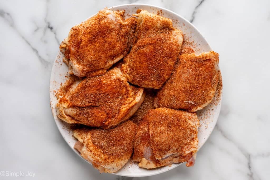 Overhead of seasoned chicken thighs on white plate to make chicken and rice