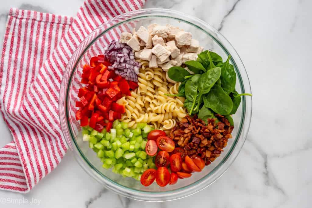 Overhead of glass bowl of chicken pasta salad ingredients with hand towel sitting under bowl