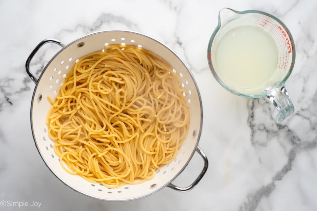 Overhead of colander of cooked pasta with glass measuring cup of pasta water sitting beside
