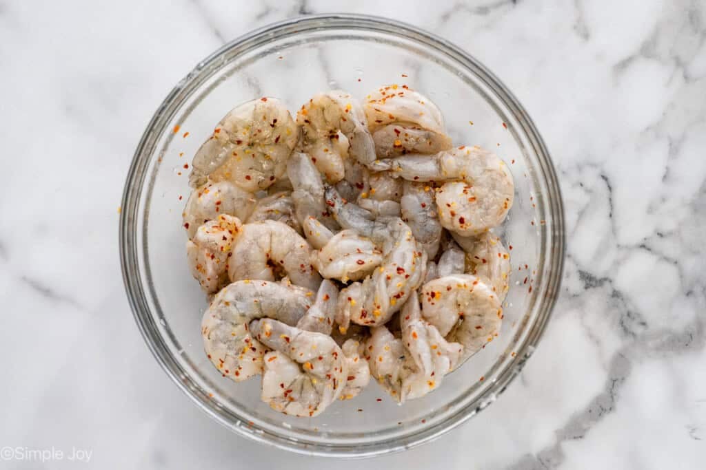 Overhead of glass bowl of raw shrimp and seasonings to make Shrimp Fra Diavolo recipe