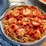 Plate of pasta topped with Shrimp Fra Diavolo and fresh parsley with a fork