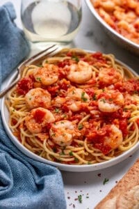Plate of pasta topped with Shrimp Fra Diavolo and fresh parsley with a fork