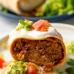 Pinterest graphic for Baked Beef and Cheese Chimichangas. Says "delicious Baked Beef and Cheese Chimichangas simplejoy.com" Image shows inside of Baked Beef and Cheese Chimichangas topped with sour cream, diced tomatoes, and guacamole